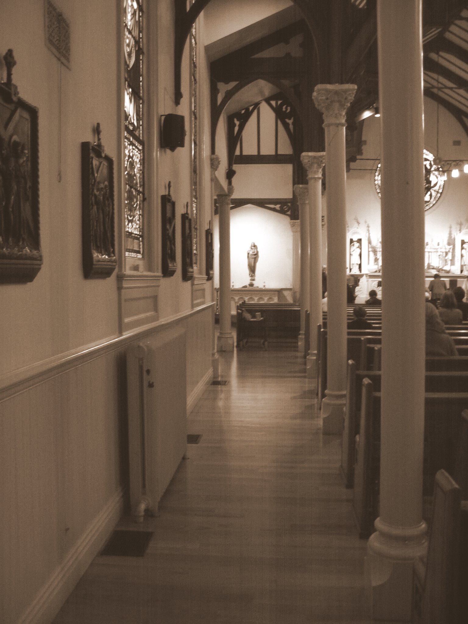 this black and white po has a view down the length line of the church, with several people seated in chairs in the rows and pictures on the wall