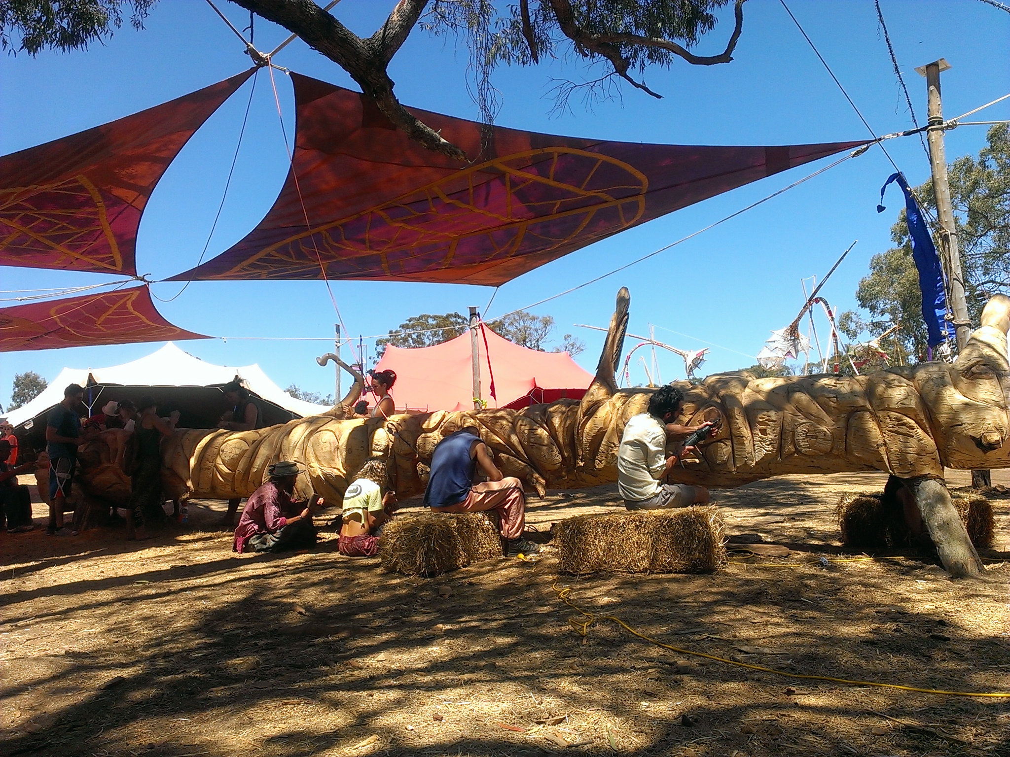 several people are preparing hay under tents on a sunny day