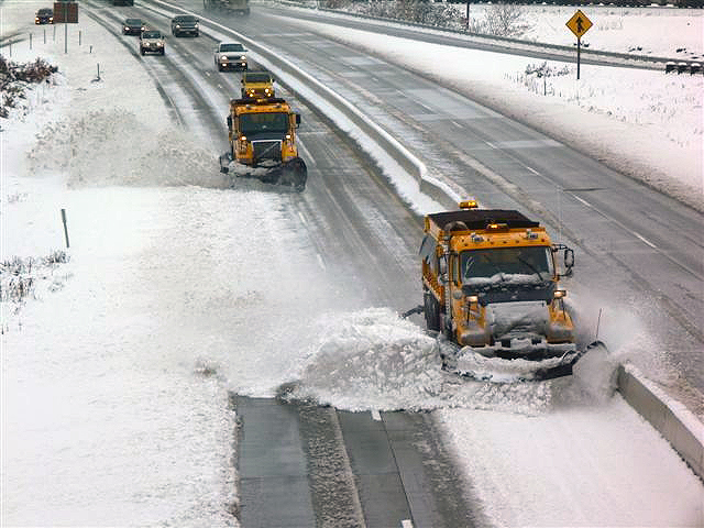 two snow plow trucks driving on a snowy road