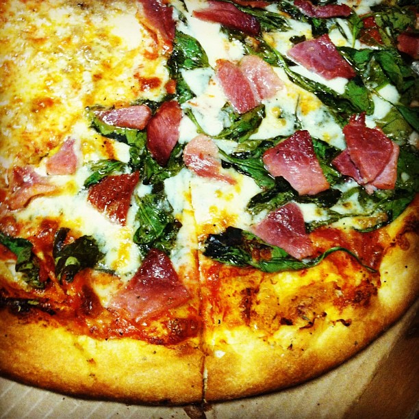 close up of a pizza with spinach and bacon on it