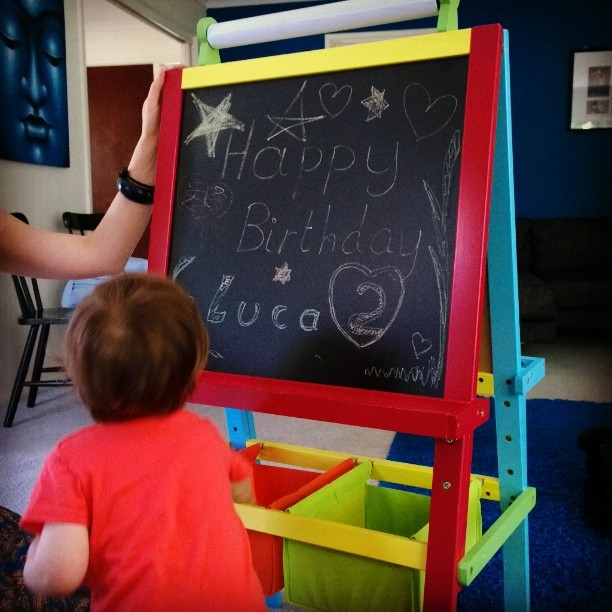 a baby is writing on the blackboard and another child is looking