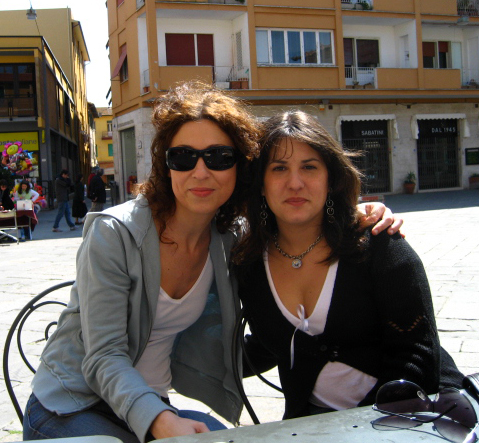 two women pose for the camera in front of some buildings