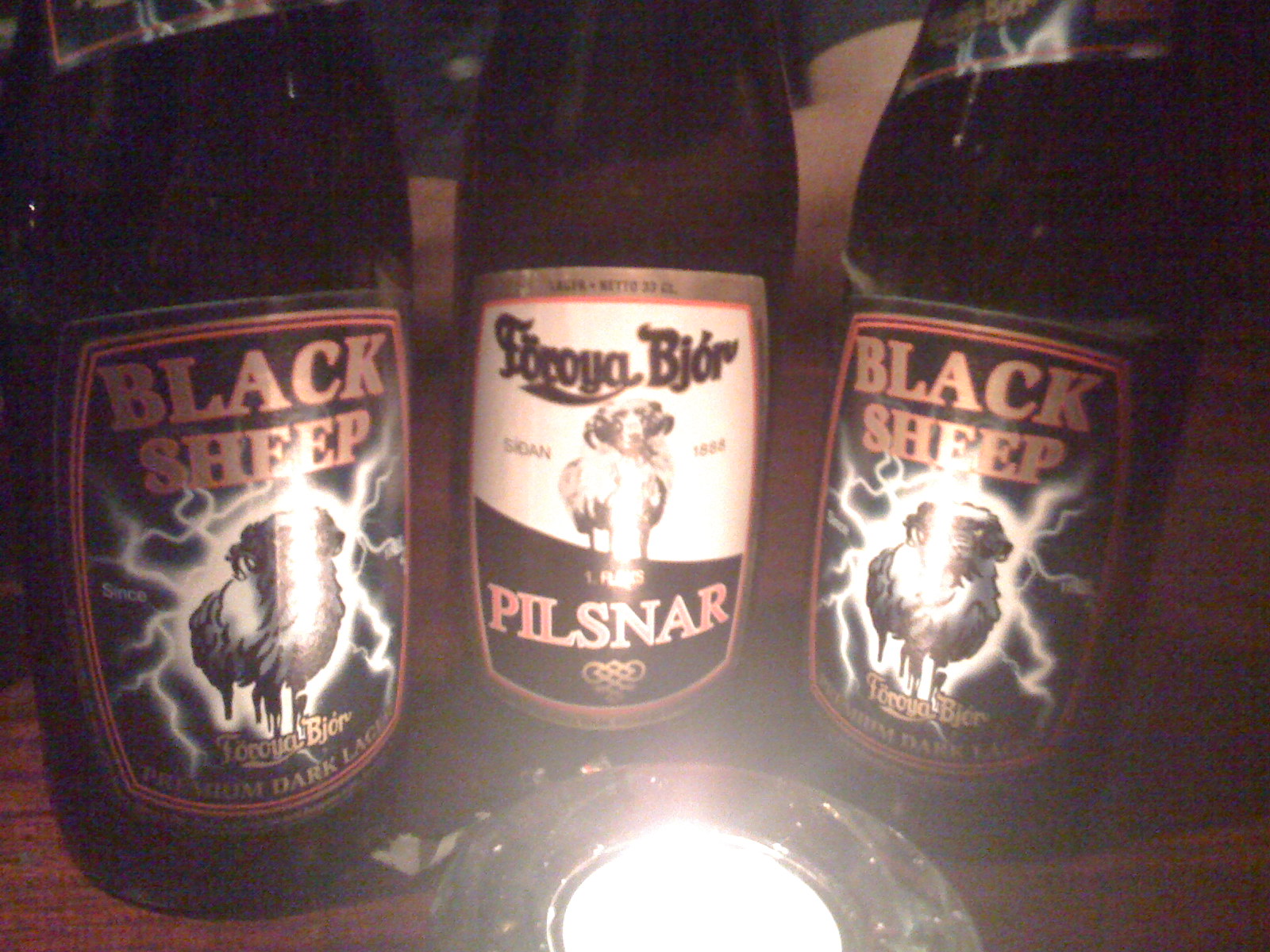 three beer bottles of black sheep pilsnar beer on a wooden table