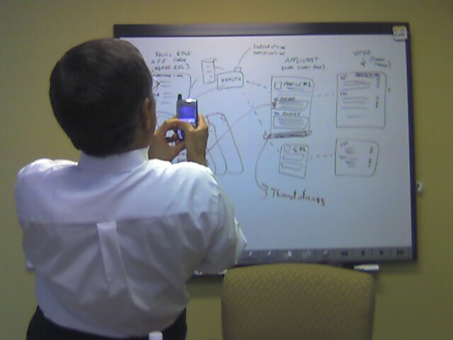 the boy is using his cell phone in front of a large whiteboard