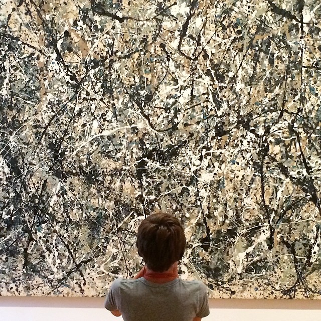 a little boy in grey shirt watching a big black and white painting