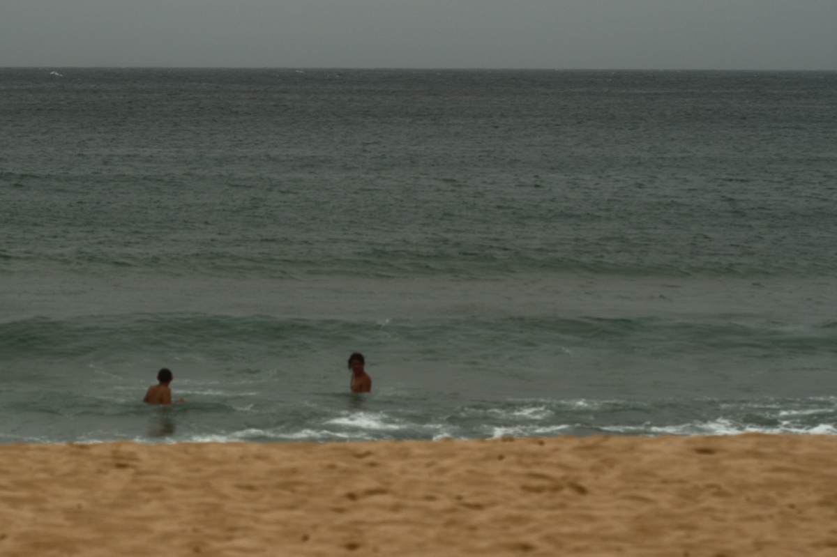 two people swim in the ocean and one is floating on a surfboard