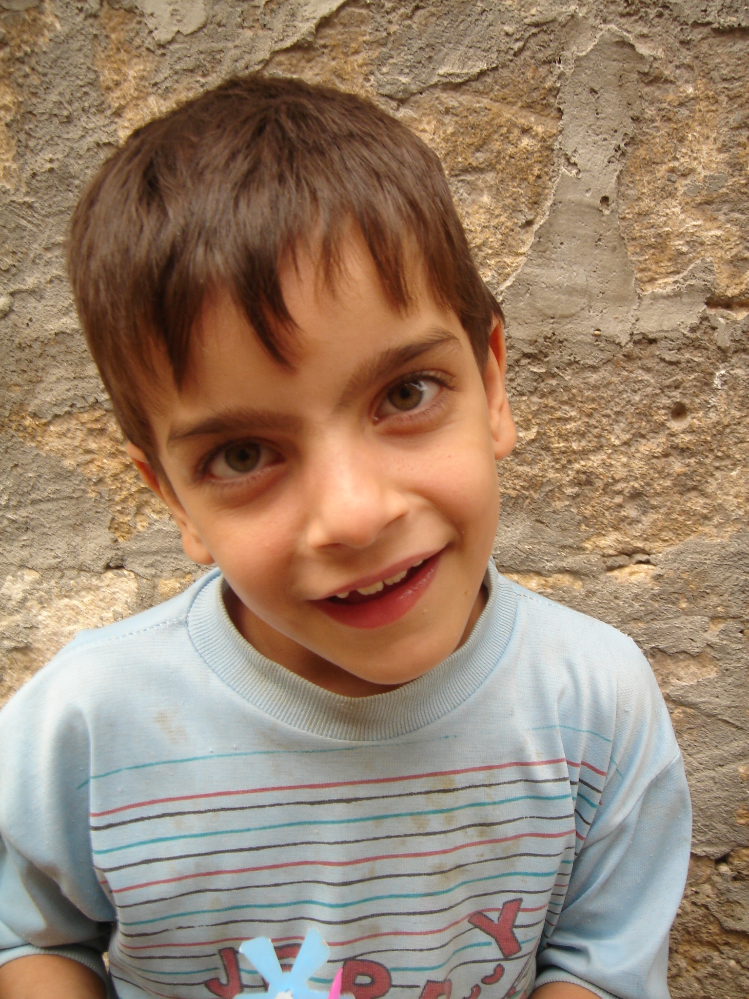 a little boy smiling in front of a stone wall