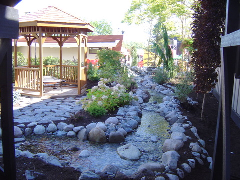 the front yard of a home features a stone garden bed and small creek