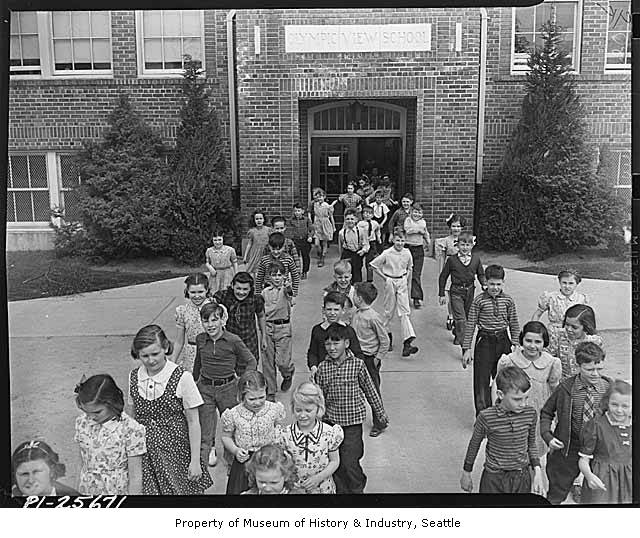 many children walking in front of a school with many children