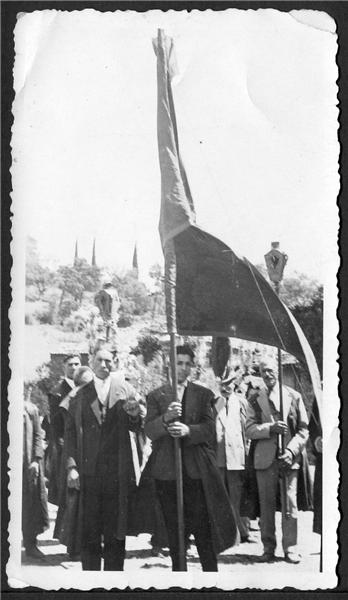 black and white pograph of men in long coats holding a flag and standing on sidewalk