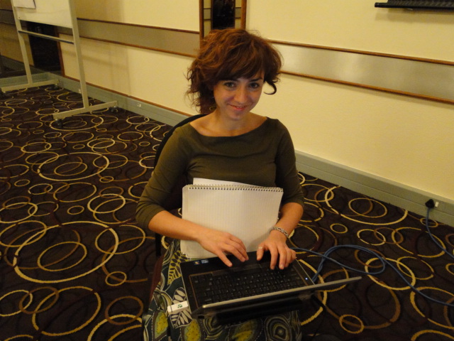 a woman wearing a green sweater is holding a black laptop