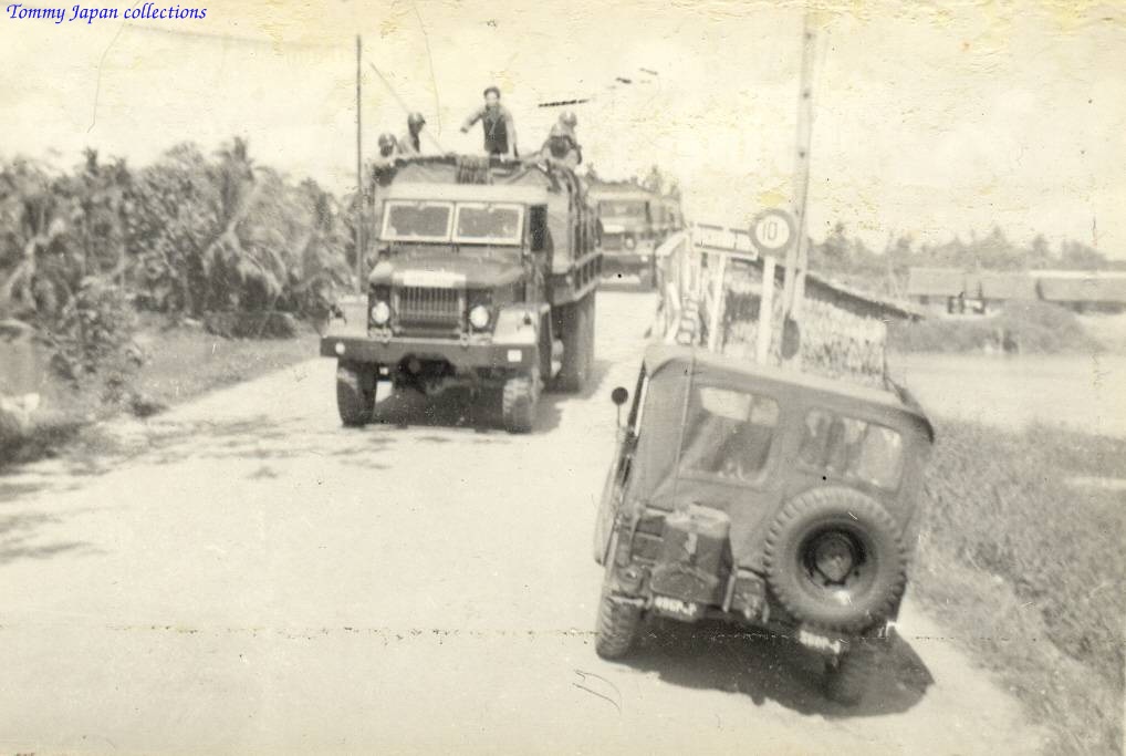 a jeep driving behind two large military vehicles