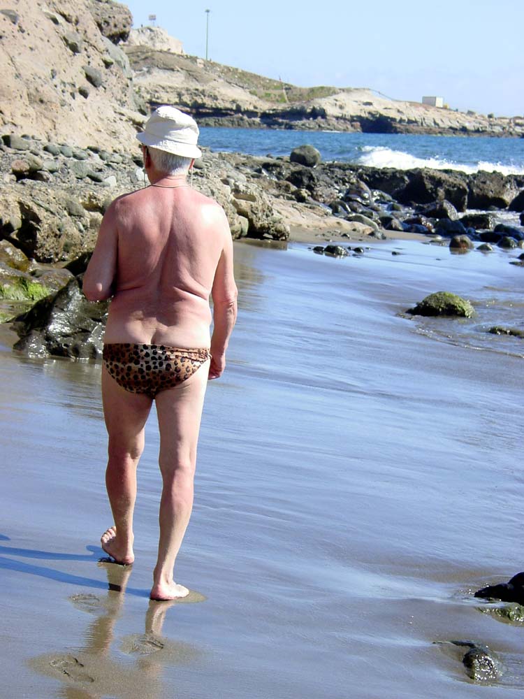 a person in leopard print swim trunks walks on the beach