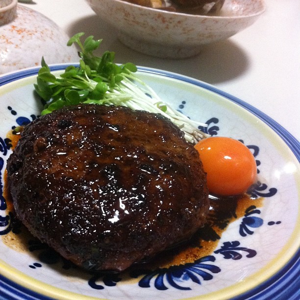 a burger with greens, an orange, and tomato on a blue and white plate
