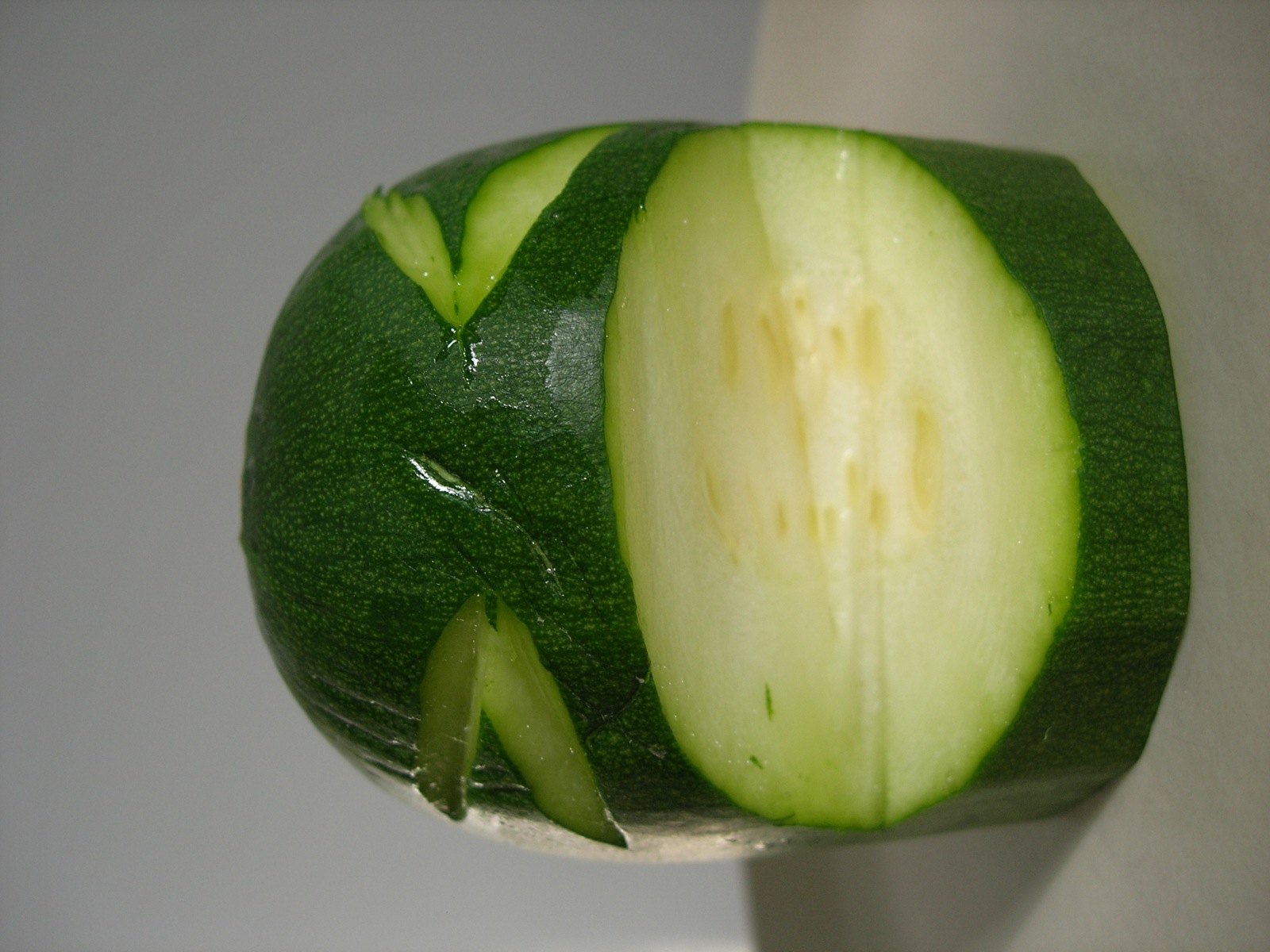 a sliced cucumber in front of a knife on a white background