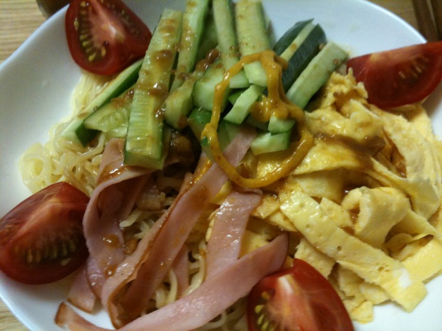 a plate with noodles, tomatoes, cucumbers and other toppings