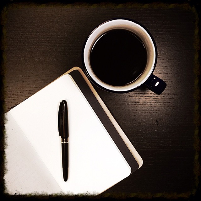 a notebook on a desk next to a cup of coffee and a pen