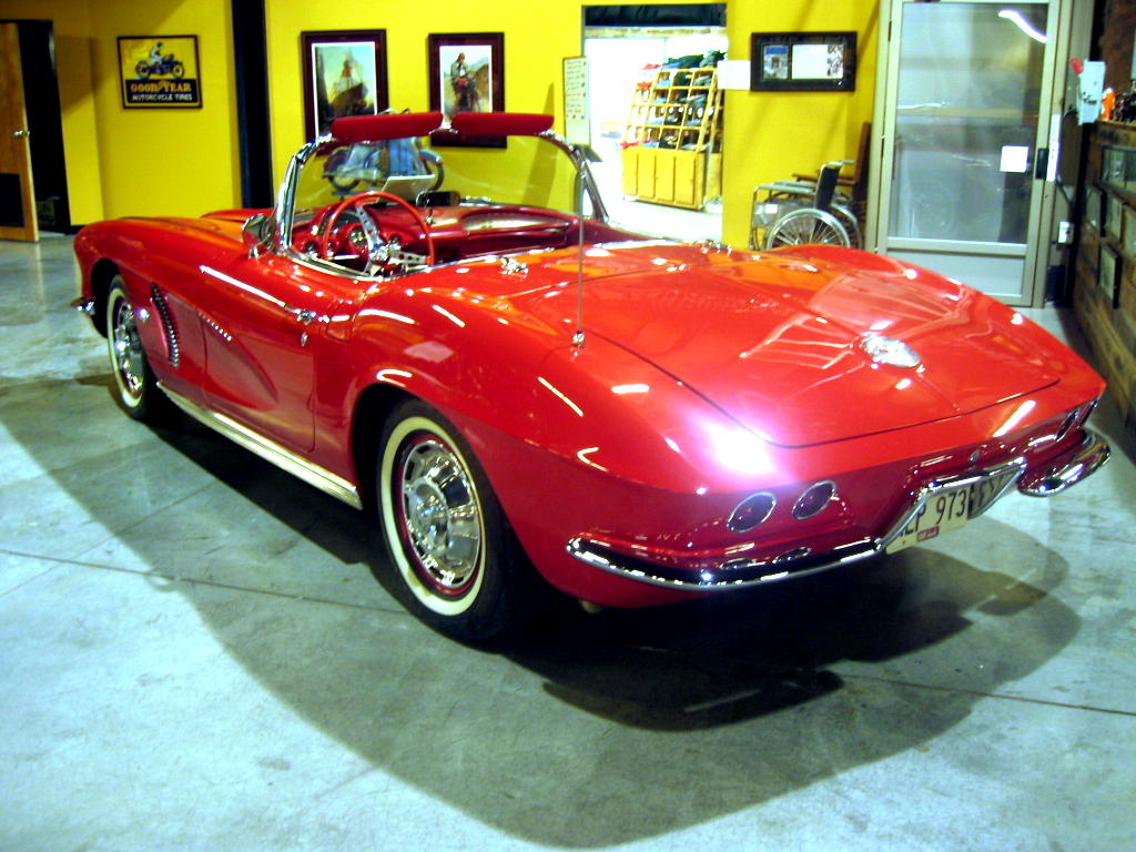 a red corvette is parked next to a yellow building