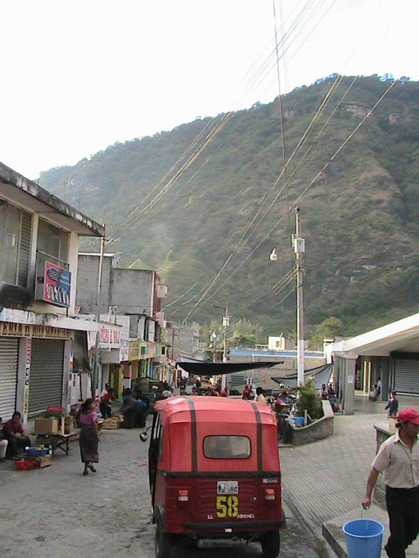 a small red van driving down a street past a man