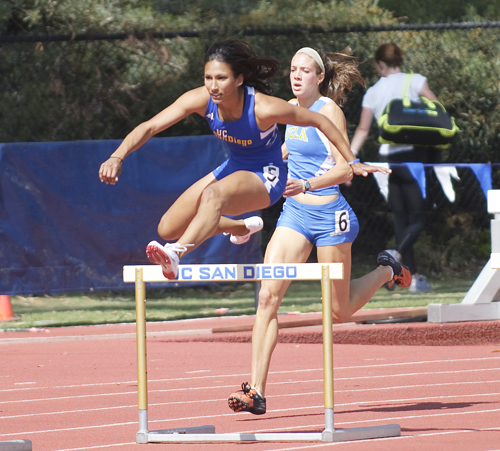 two girls competing in a race jumping over hurdles