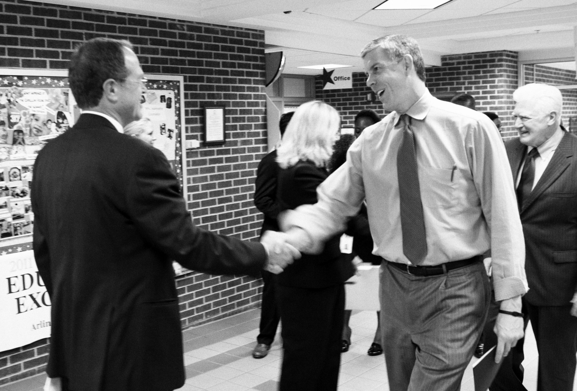 two men in business suits shaking hands in an office hallway