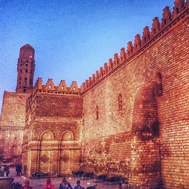 the night scene of a very old castle like structure with people standing outside it