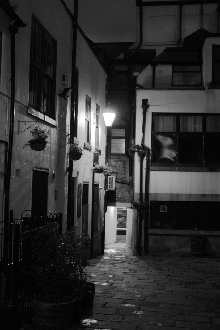 a narrow city alley with two bricked buildings at night