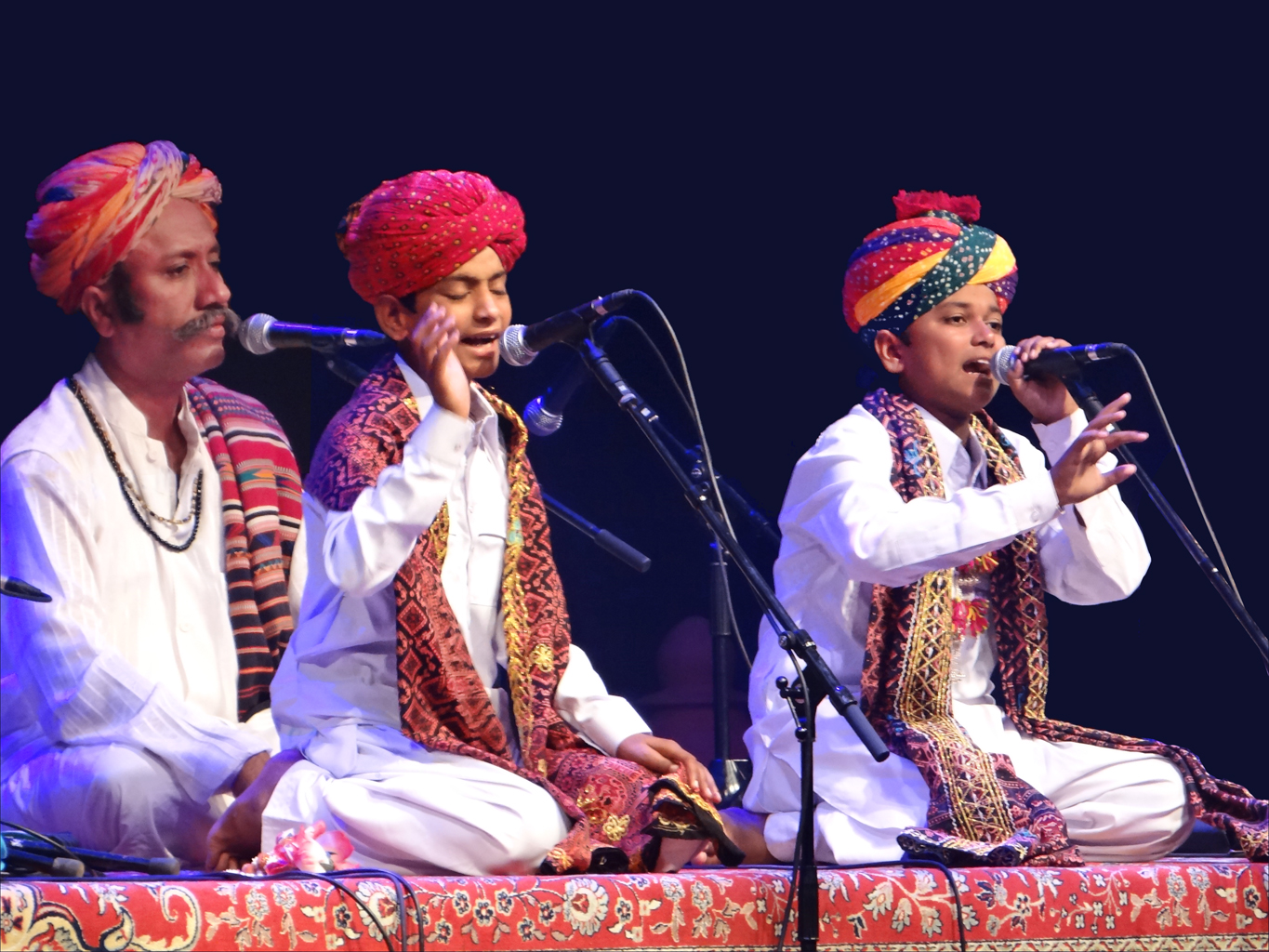 two men in turbans sit on stage while singing