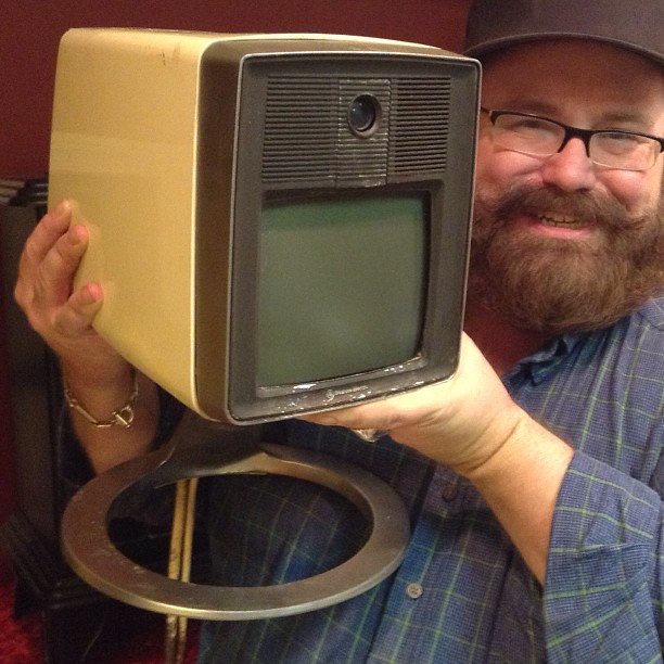 a man holds a large retro tv with an oversized wheel