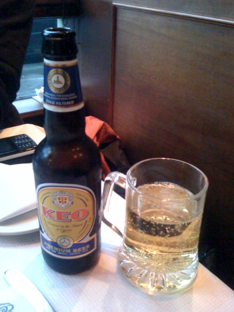 an unopened glass of beer next to a large bottle of beer on the table