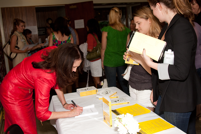 a woman in red and black signing papers next to a table