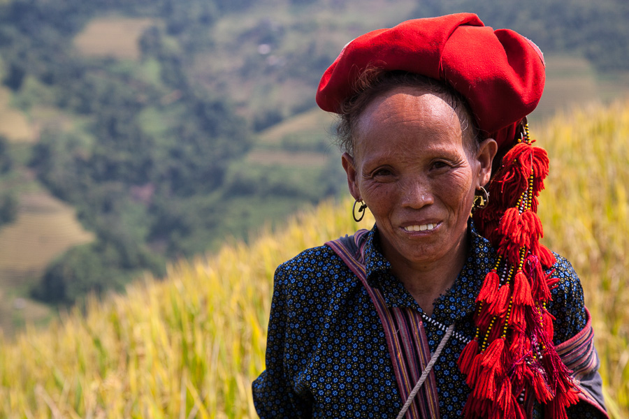 a woman with a red hat on her head standing in front of some wheat field