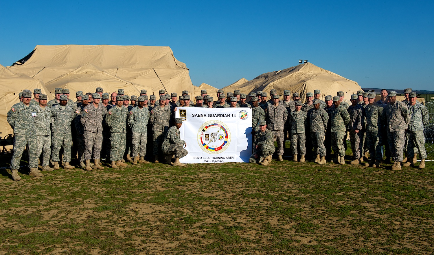 a large group of military people are posing in front of a backdrop of sand