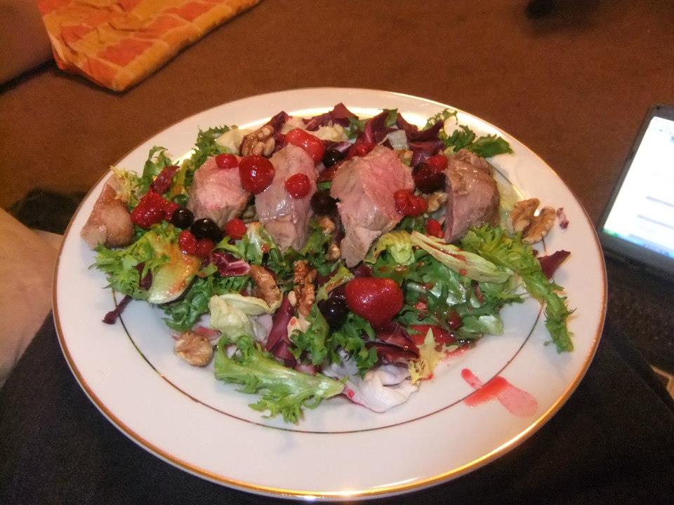 a white plate topped with meat and salad next to a laptop