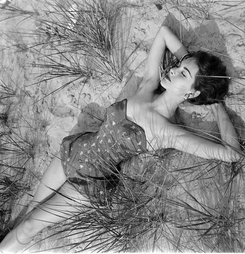a woman laying in some sand and some plants
