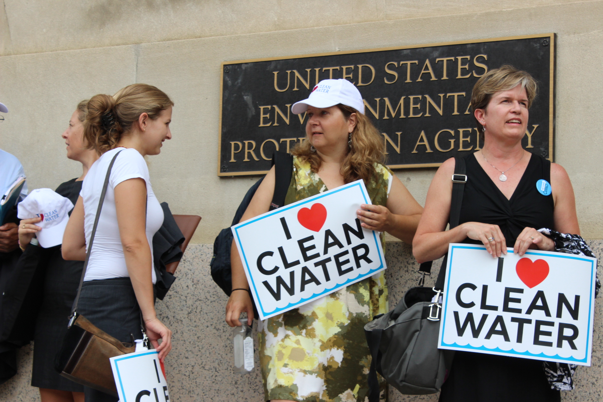 a group of women standing outside a building holding clean water signs