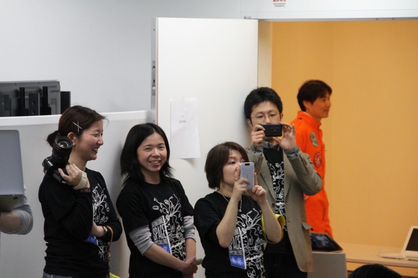 an asian group standing next to a white wall holding up their cellphones