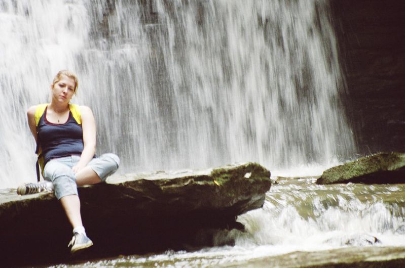 a girl is sitting on a rock next to a waterfall