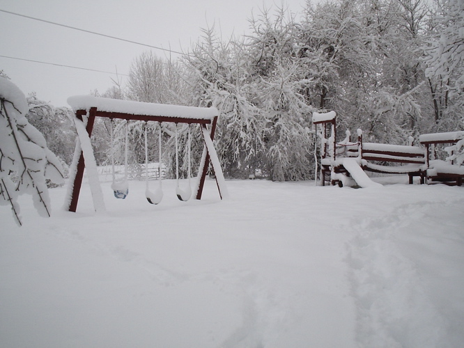 two swings in the snow with trees and buildings