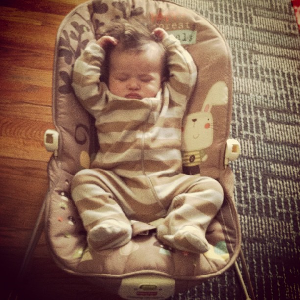 a baby sleeping in a baby chair, wearing a striped outfit