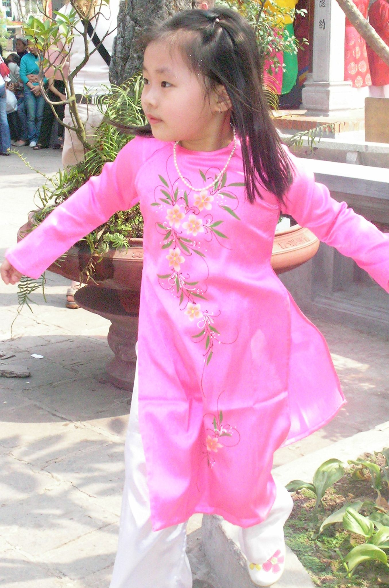 a little girl in a pink dress and white pants