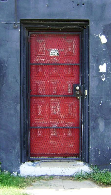 a red door is behind bars of wire on a grey building