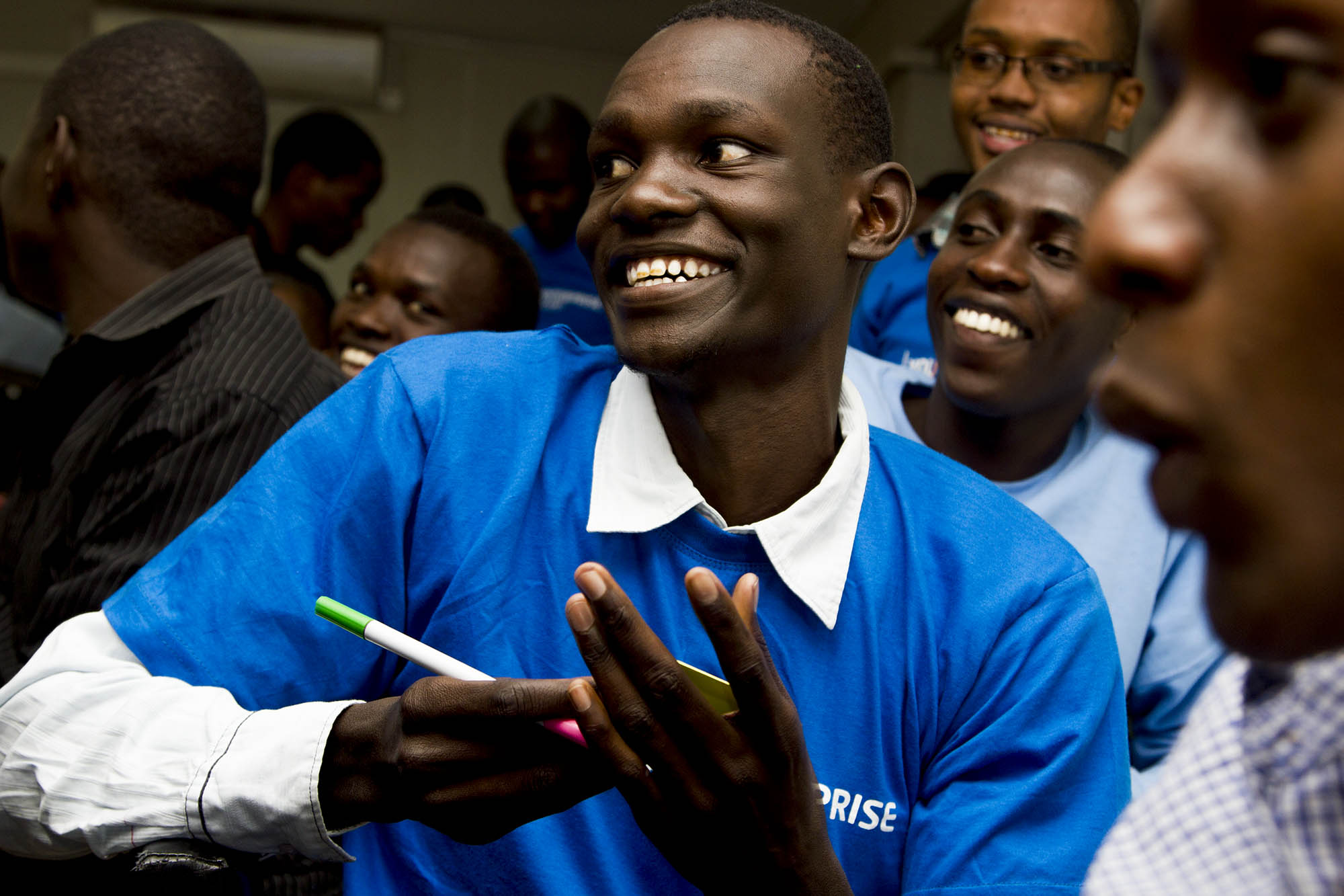 a man wearing a blue shirt smiling and holding a pen in front of other men