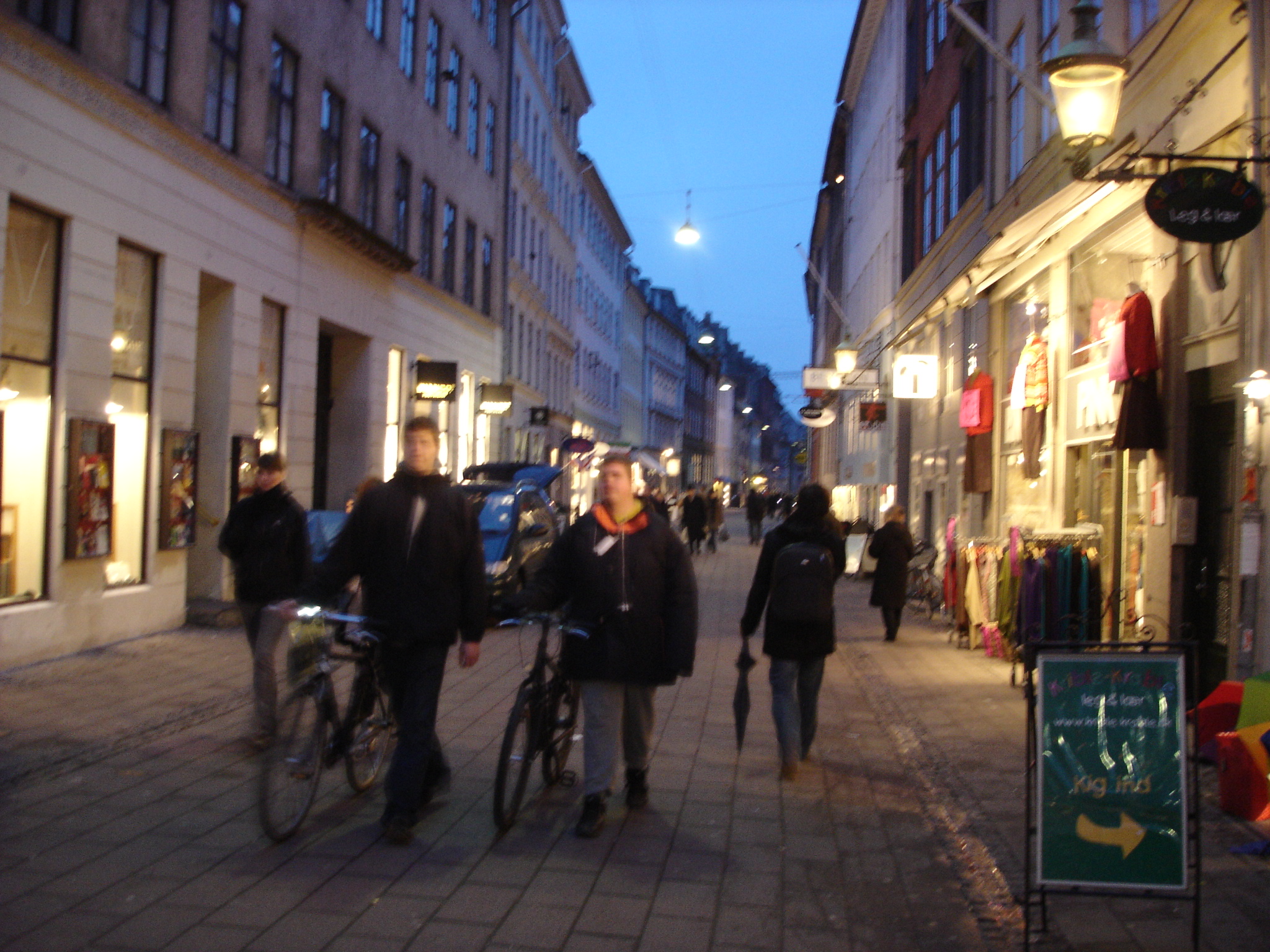 several people walking down a sidewalk in the evening