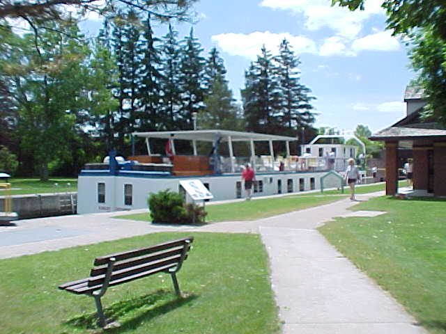 a long boat at the end of a river near a park bench