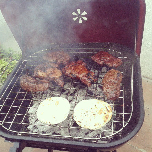 a bbq grill with meat and two tortillas cooking on it