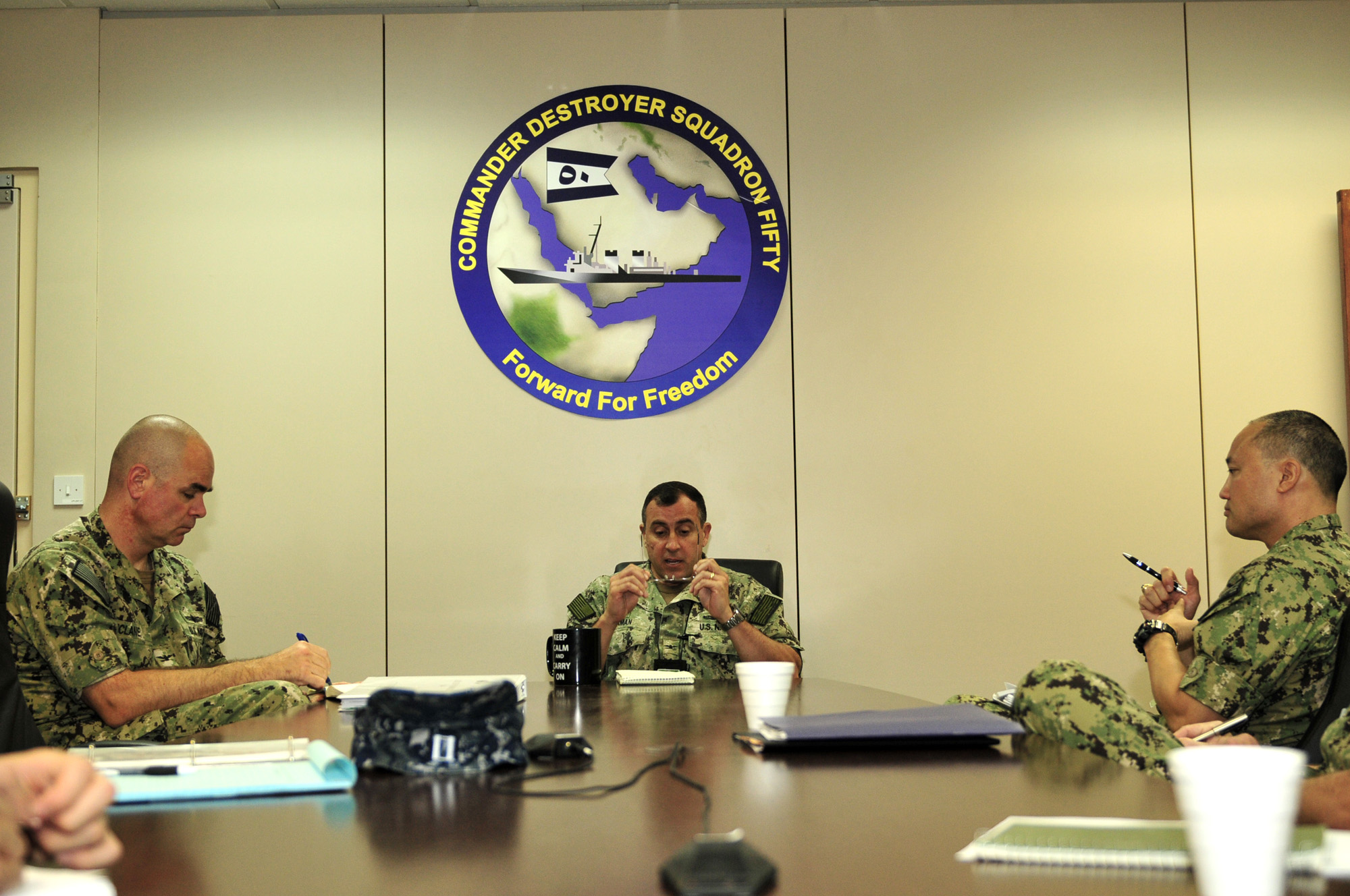 four men sitting at a table and one man on his phone