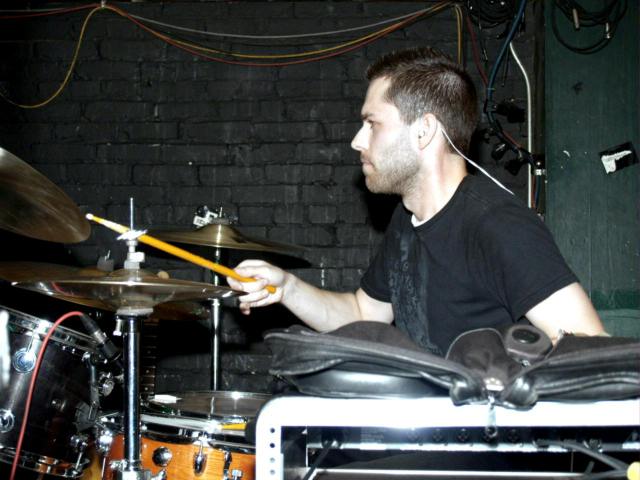 a man with ear buds on drumming while playing a set