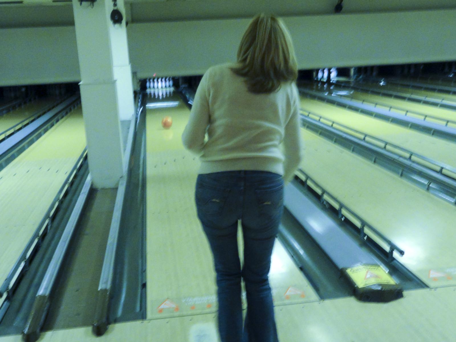 a woman in white sweater and jeans walking next to bowling alleys