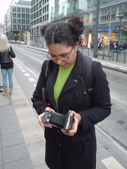 a woman looking at a cellphone while standing on the sidewalk